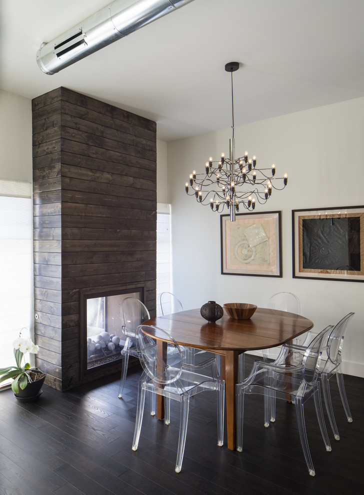 Cette photo montre une salle à manger ouverte sur le salon moderne de taille moyenne avec parquet foncé, une cheminée double-face, un manteau de cheminée en bois et un mur beige.
