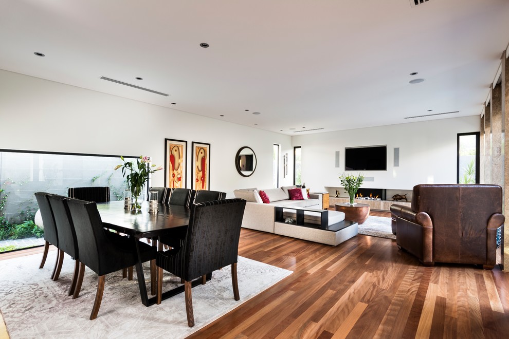 Réalisation d'une salle à manger ouverte sur le salon design de taille moyenne avec un mur blanc, un sol en bois brun, une cheminée standard, un manteau de cheminée en plâtre et un sol marron.