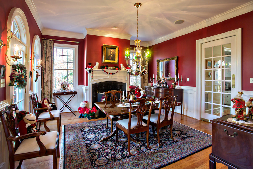 Exemple d'une salle à manger chic avec un mur rouge, un sol en bois brun et une cheminée standard.