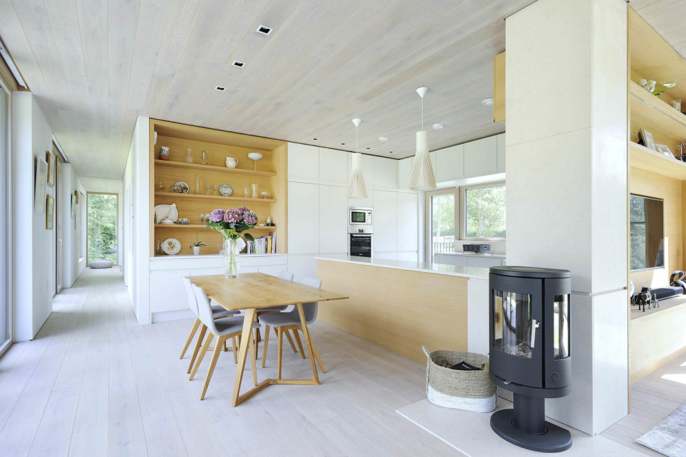 Exemple d'une grande salle à manger ouverte sur la cuisine tendance avec un mur blanc, un poêle à bois, un manteau de cheminée en métal et un sol gris.