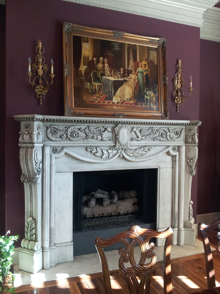 Cette photo montre une grande salle à manger ouverte sur le salon chic avec un mur violet, un sol en bois brun, une cheminée standard et un manteau de cheminée en pierre.