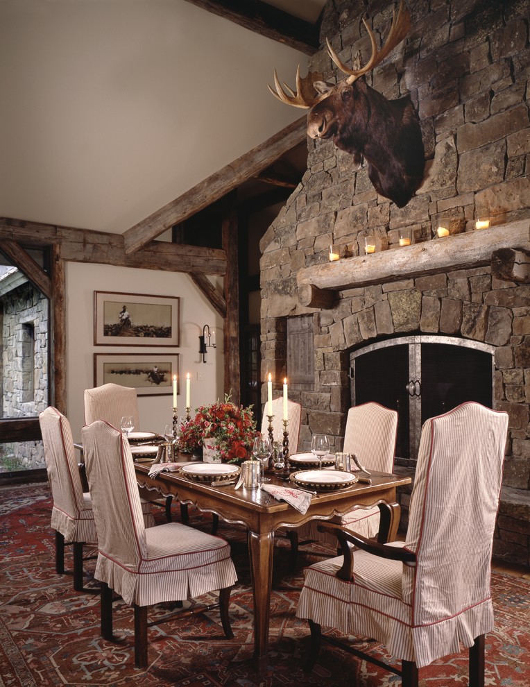 Inspiration pour une salle à manger chalet avec un mur blanc, une cheminée standard et un manteau de cheminée en pierre.