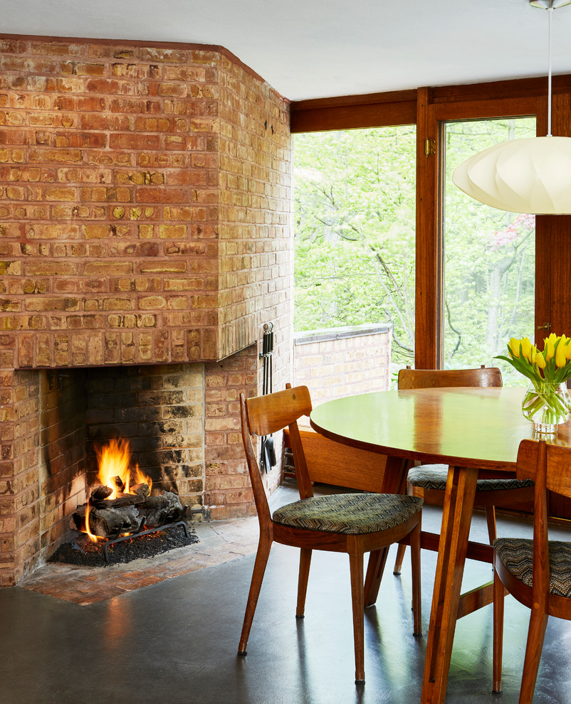 Cette image montre une petite salle à manger ouverte sur la cuisine vintage avec sol en béton ciré, une cheminée d'angle et un manteau de cheminée en brique.