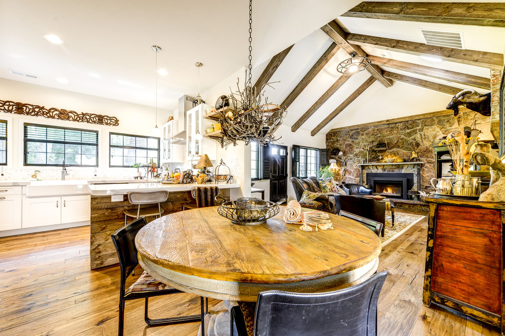 Inspiration for a medium sized rustic kitchen/dining room in Denver with white walls, medium hardwood flooring, a standard fireplace, a stone fireplace surround and brown floors.