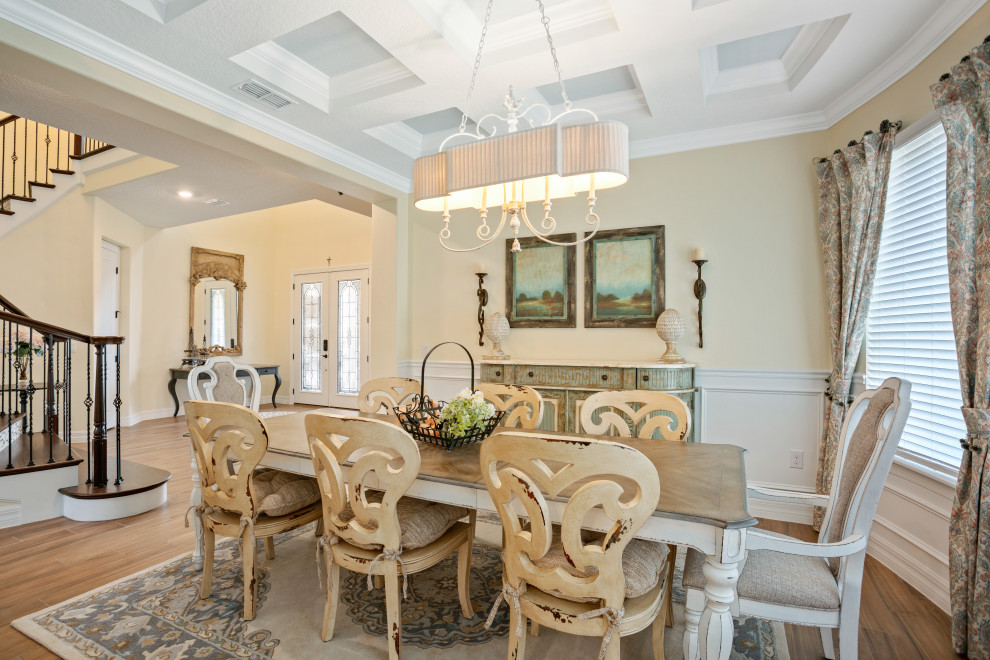 French country light wood floor, coffered ceiling and wainscoting dining room photo in Orlando