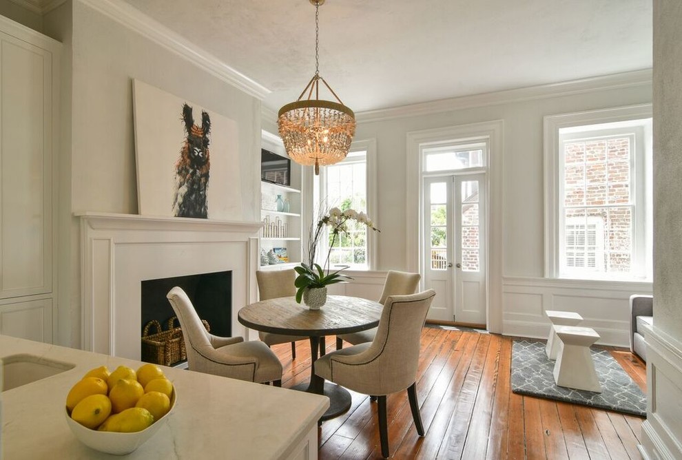 This is an example of a traditional dining room in Charleston with white walls, medium hardwood flooring, a standard fireplace and brown floors.