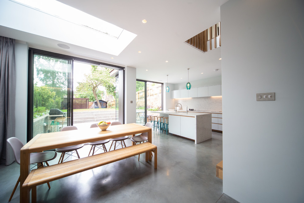 Cette photo montre une salle à manger ouverte sur la cuisine moderne de taille moyenne avec un mur blanc, sol en béton ciré et un sol gris.