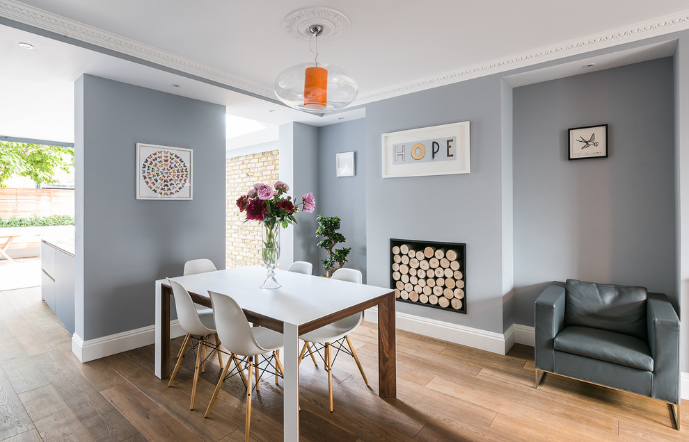 Inspiration pour une salle à manger ouverte sur le salon design avec un sol en bois brun, une cheminée standard et un mur gris.