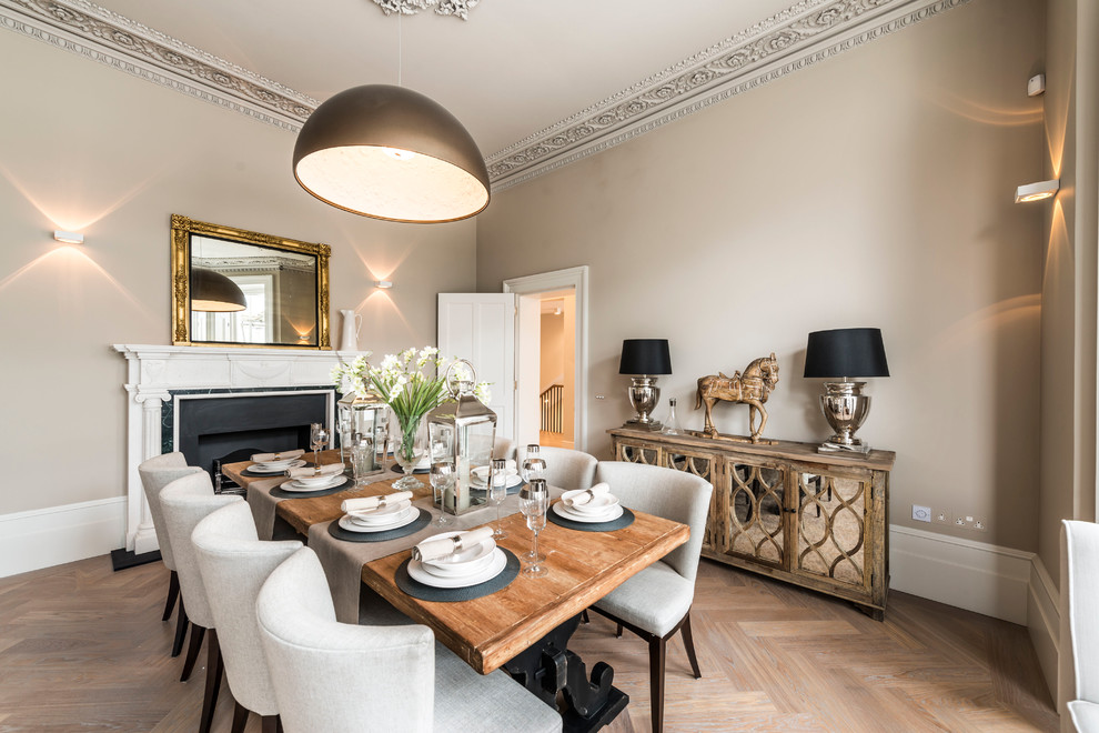 Photo of a traditional enclosed dining room in London with beige walls, light hardwood flooring, a standard fireplace and feature lighting.