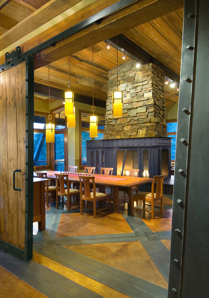 Cette photo montre une grande salle à manger montagne fermée avec un mur beige, sol en béton ciré, un poêle à bois, un sol multicolore et un manteau de cheminée en métal.