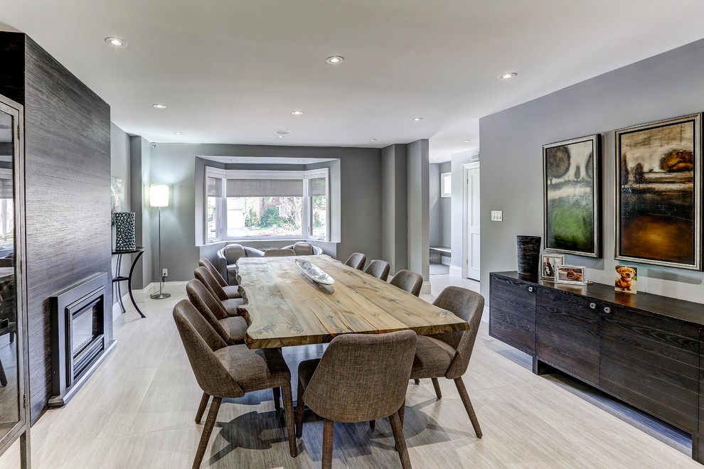 Photo of an expansive contemporary kitchen/dining room in Toronto with grey walls, porcelain flooring, a standard fireplace, a tiled fireplace surround and grey floors.