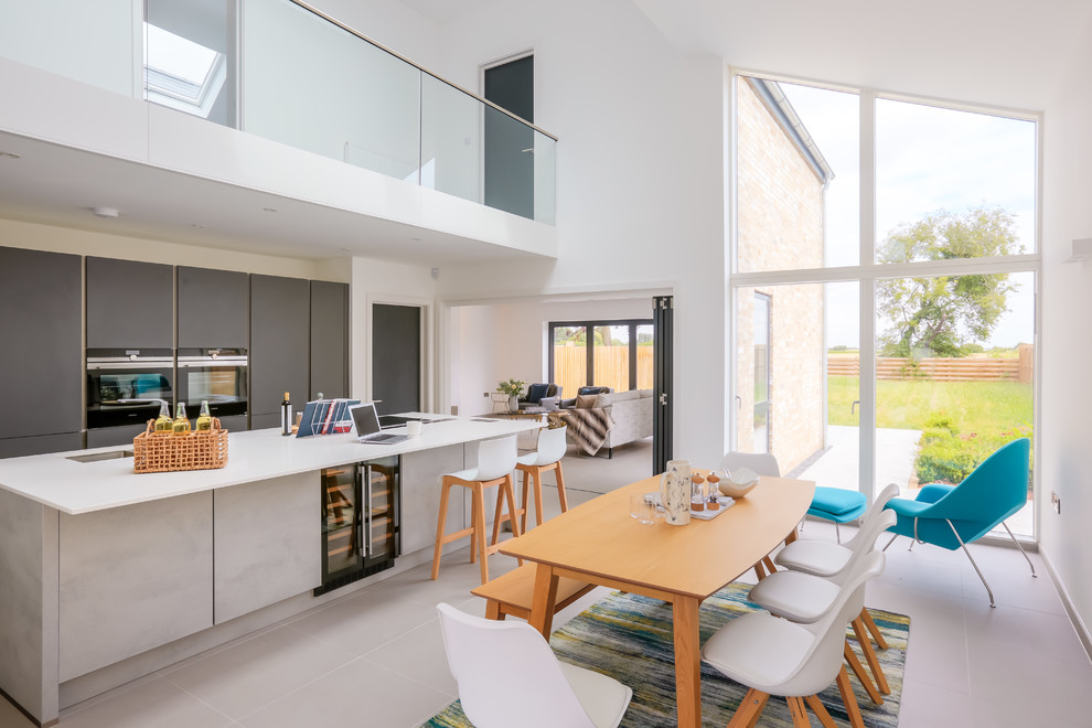 Cette image montre une salle à manger ouverte sur la cuisine design avec un mur blanc, aucune cheminée et un sol gris.
