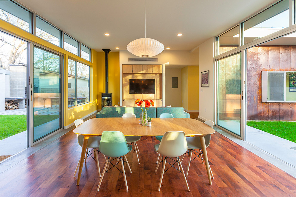 Idée de décoration pour une salle à manger ouverte sur le salon vintage avec un mur jaune, parquet foncé et un poêle à bois.