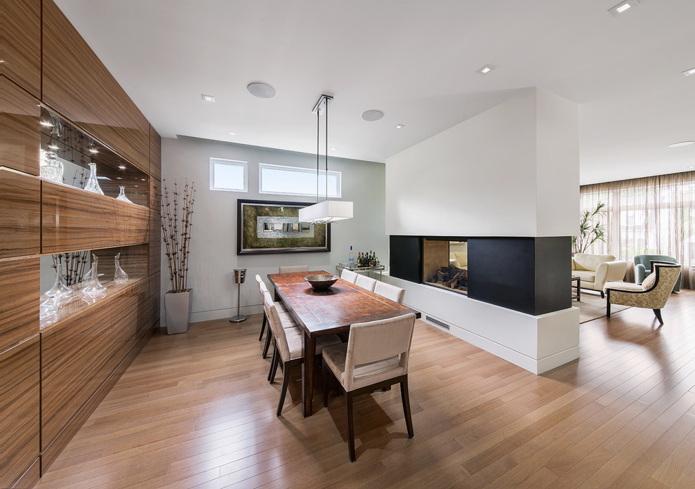 Idée de décoration pour une salle à manger design avec un mur blanc, un sol en bois brun et une cheminée double-face.