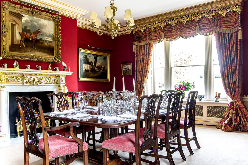 This is an example of a medium sized traditional dining room in London with red walls, carpet, a standard fireplace and beige floors.