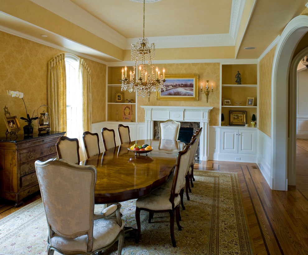 Immagine di una sala da pranzo tradizionale chiusa e di medie dimensioni con pareti gialle, parquet chiaro e camino classico