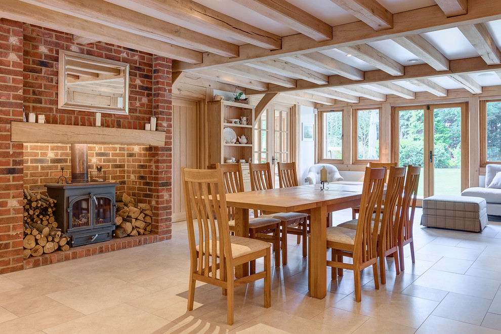 Cette photo montre une salle à manger ouverte sur le salon nature avec un poêle à bois, un manteau de cheminée en brique et un sol beige.