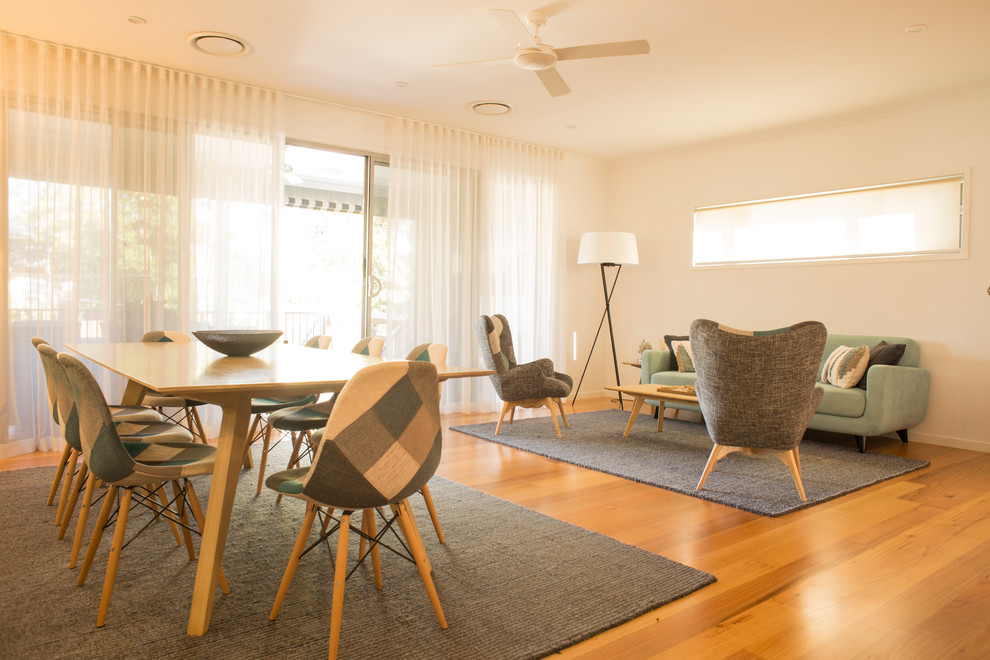 На фото: большая гостиная-столовая в стиле модернизм с белыми стенами, полом из ламината и коричневым полом