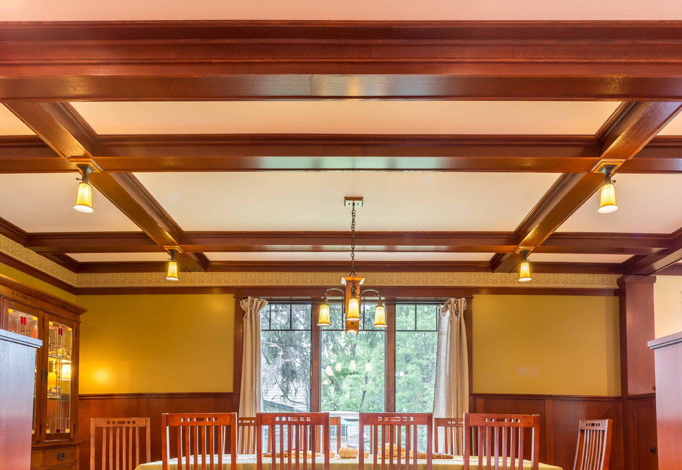 Esempio di una sala da pranzo aperta verso il soggiorno american style di medie dimensioni con pareti gialle, parquet chiaro, nessun camino, pavimento marrone, soffitto a cassettoni e boiserie