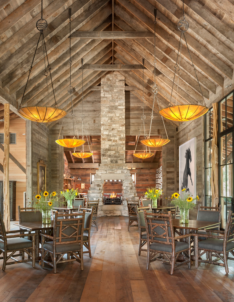 Rustic open plan dining room in Austin with a two-sided fireplace and a stone fireplace surround.