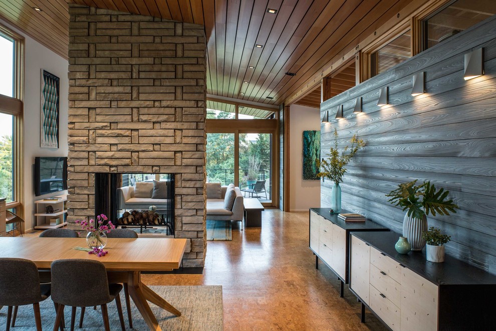 Cette image montre une salle à manger ouverte sur la cuisine design de taille moyenne avec un mur gris, parquet en bambou, une cheminée double-face, un manteau de cheminée en pierre et un sol beige.