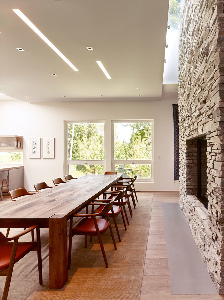 Источник вдохновения для домашнего уюта: большая кухня-столовая в современном стиле с белыми стенами, светлым паркетным полом, двусторонним камином, фасадом камина из камня и коричневым полом