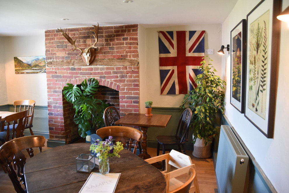 Inspiration pour une salle à manger rustique fermée et de taille moyenne avec un mur vert, sol en stratifié, une cheminée standard, un manteau de cheminée en brique et un sol marron.