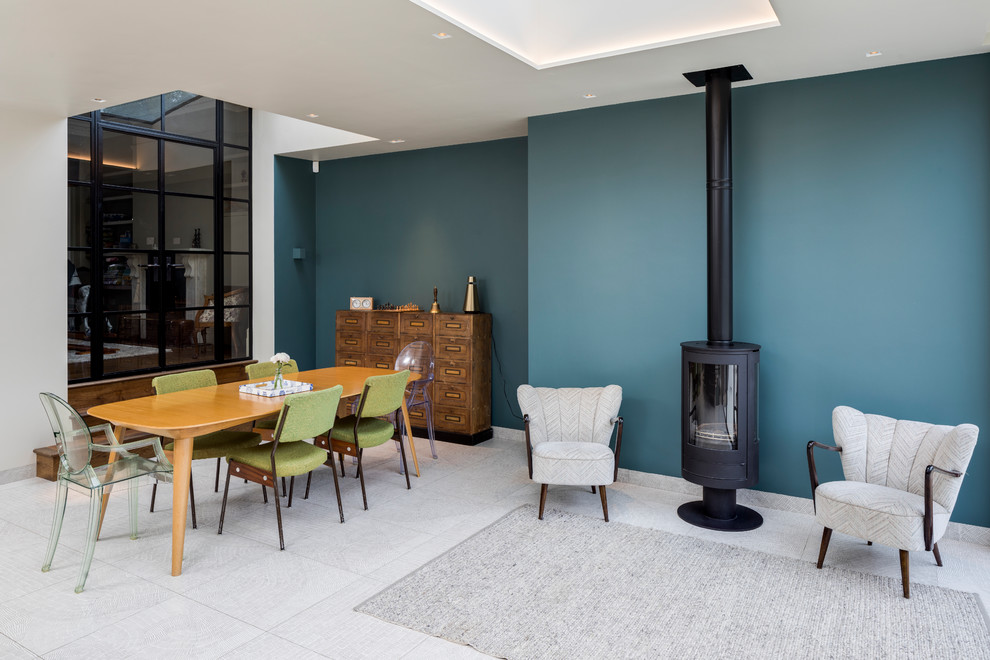 Immagine di una sala da pranzo aperta verso il soggiorno minimal con pareti blu, stufa a legna, cornice del camino in metallo e pavimento grigio