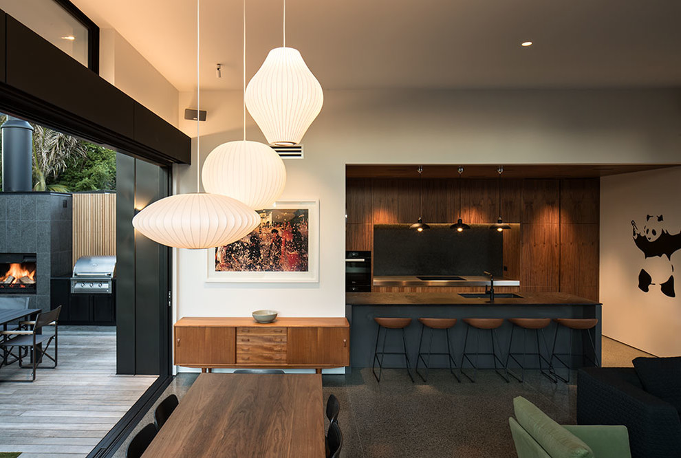 Idées déco pour une salle à manger ouverte sur la cuisine rétro de taille moyenne avec un mur blanc, sol en béton ciré, une cheminée d'angle et un manteau de cheminée en pierre.