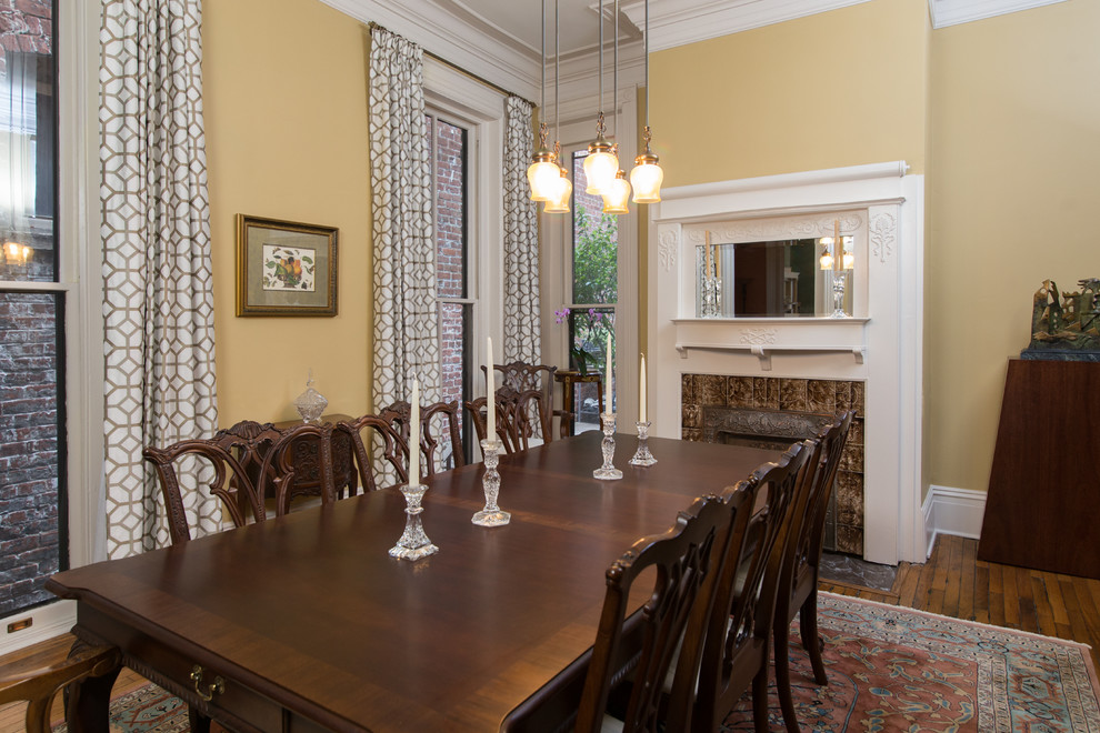 Immagine di una grande sala da pranzo classica chiusa con pareti gialle, pavimento in legno massello medio, camino classico, cornice del camino piastrellata e pavimento marrone