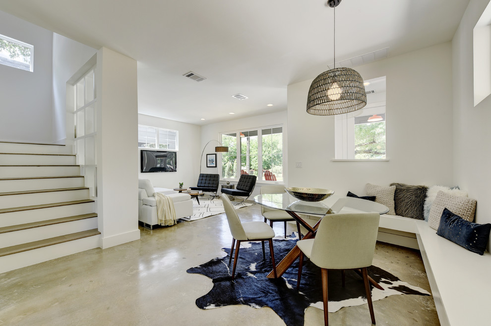 Cette image montre une petite salle à manger ouverte sur la cuisine minimaliste avec un mur blanc, sol en béton ciré, aucune cheminée et éclairage.