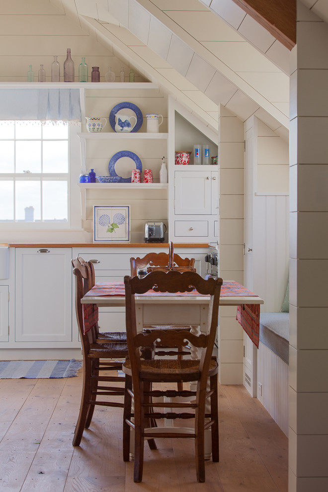 Aménagement d'une salle à manger ouverte sur la cuisine bord de mer de taille moyenne avec un mur blanc, un sol en bois brun, une cheminée standard et un manteau de cheminée en pierre.