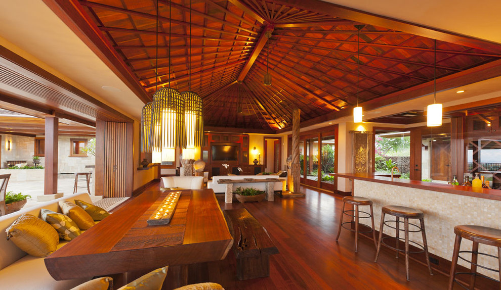 Immagine di una grande sala da pranzo aperta verso il soggiorno tropicale con pareti beige, pavimento in legno massello medio e nessun camino