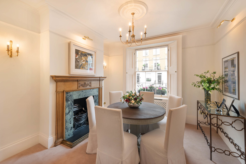 This is an example of a medium sized traditional dining room in London with beige walls, carpet, a standard fireplace and beige floors.