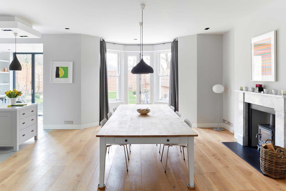 Ispirazione per una sala da pranzo aperta verso la cucina minimalista di medie dimensioni con pareti grigie, parquet chiaro, stufa a legna e cornice del camino in pietra