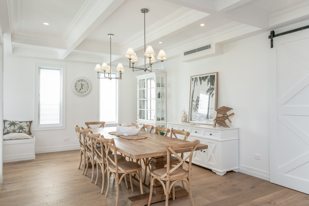 Idées déco pour une salle à manger ouverte sur la cuisine bord de mer de taille moyenne avec un mur blanc, un sol en bois brun, une cheminée standard, un sol marron et un plafond à caissons.