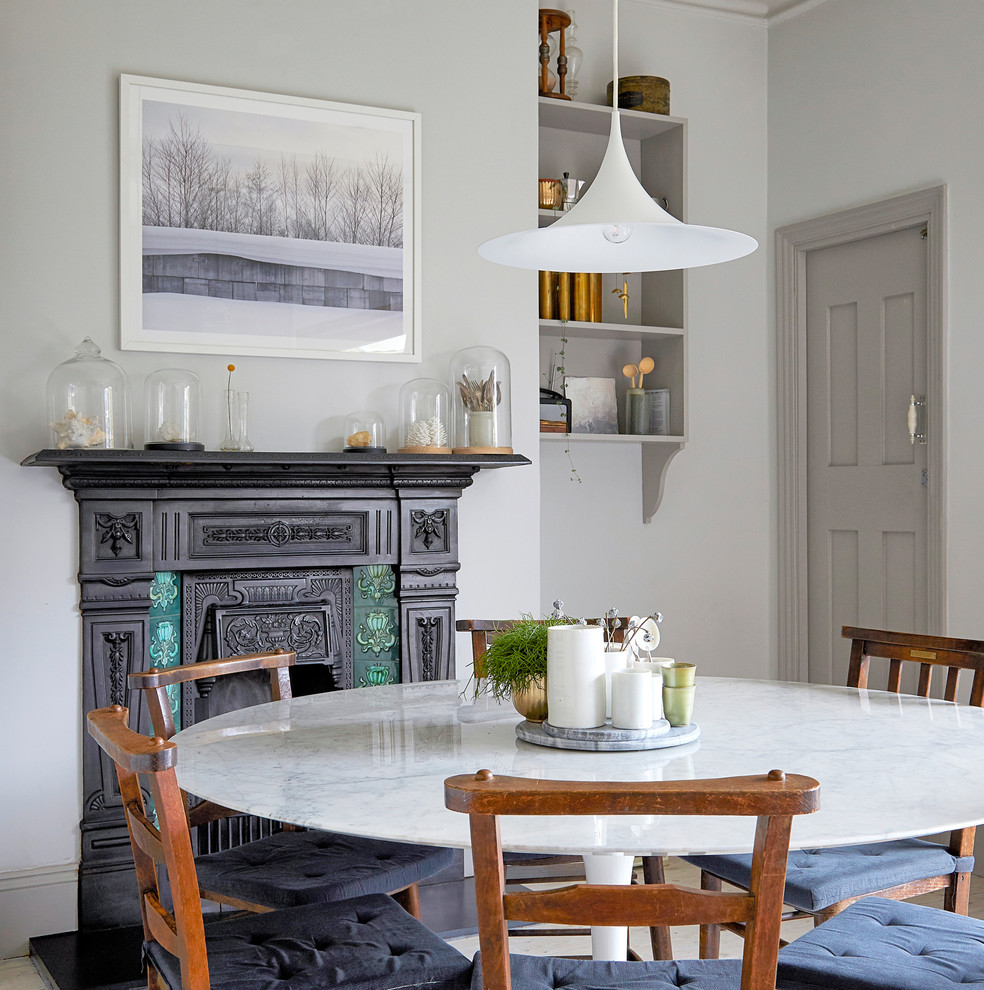 Mid-sized ornate painted wood floor and white floor kitchen/dining room combo photo in London with gray walls, a standard fireplace and a metal fireplace