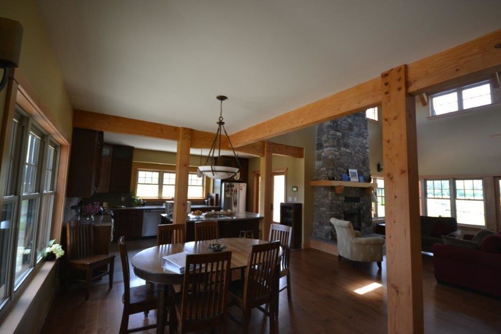 Cette photo montre une grande salle à manger ouverte sur la cuisine chic avec un mur beige, un sol en bois brun, une cheminée standard et un manteau de cheminée en pierre.