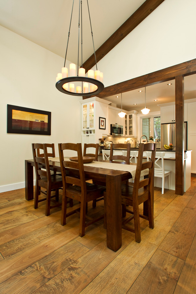 Cette photo montre une salle à manger ouverte sur la cuisine chic avec un mur blanc et un sol en bois brun.