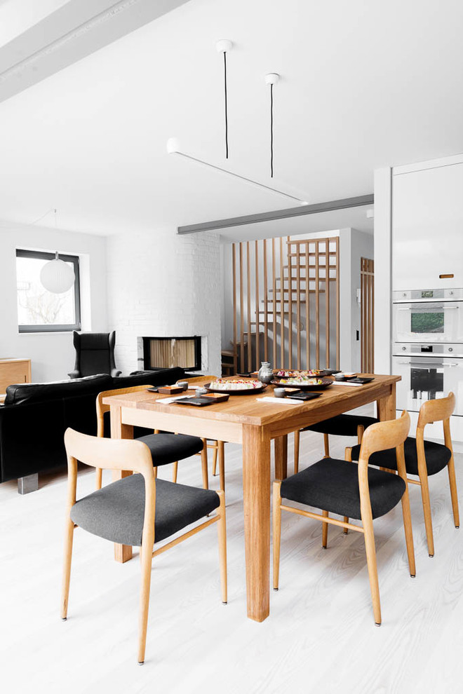Inspiration pour une salle à manger ouverte sur le salon nordique de taille moyenne avec un mur blanc, parquet clair, une cheminée d'angle et un manteau de cheminée en brique.