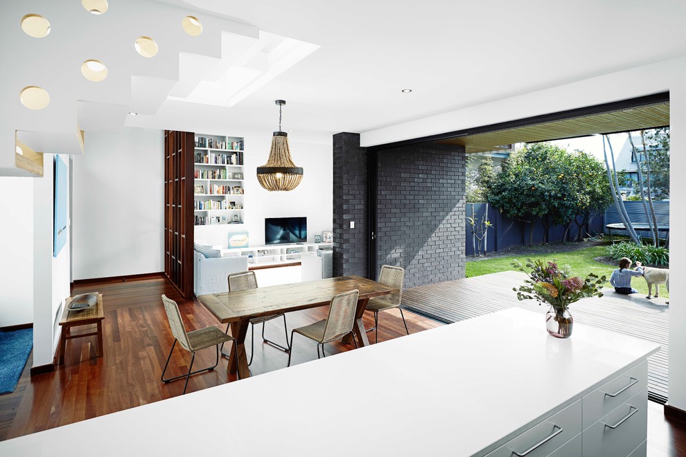 Cette photo montre une salle à manger ouverte sur le salon tendance de taille moyenne avec un mur blanc, parquet foncé, aucune cheminée, un sol marron et un mur en parement de brique.
