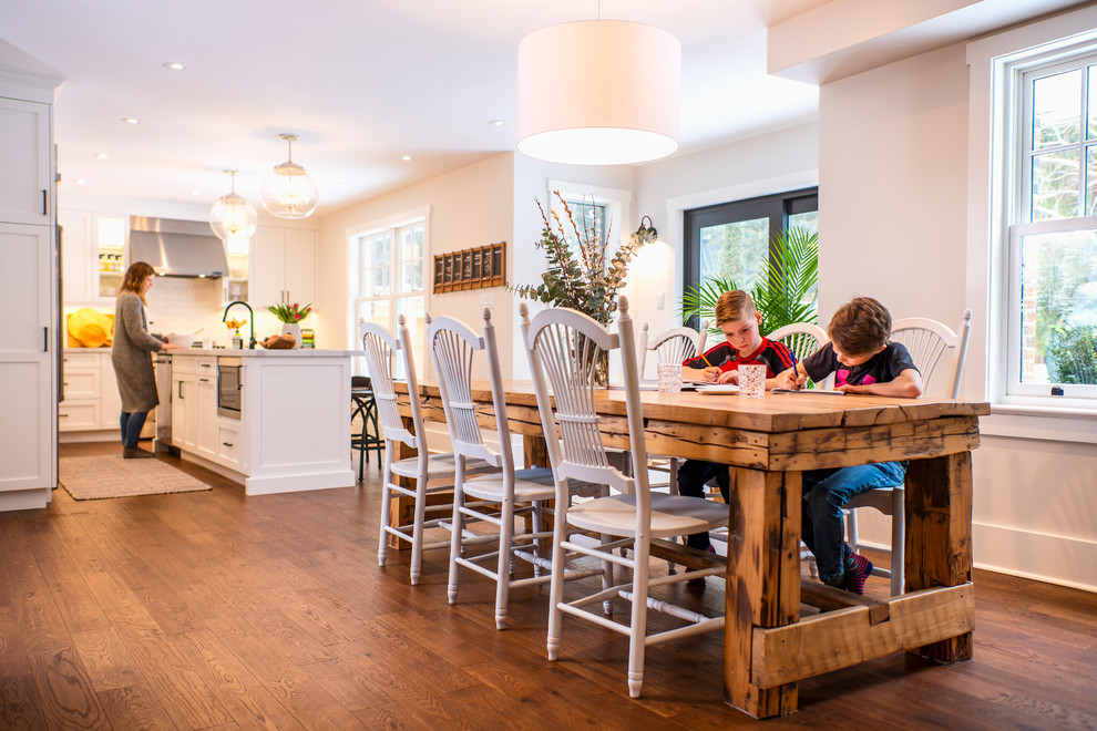 Inspiration pour une salle à manger ouverte sur la cuisine minimaliste de taille moyenne avec un mur blanc, un sol en bois brun, une cheminée double-face, un manteau de cheminée en plâtre et un sol marron.