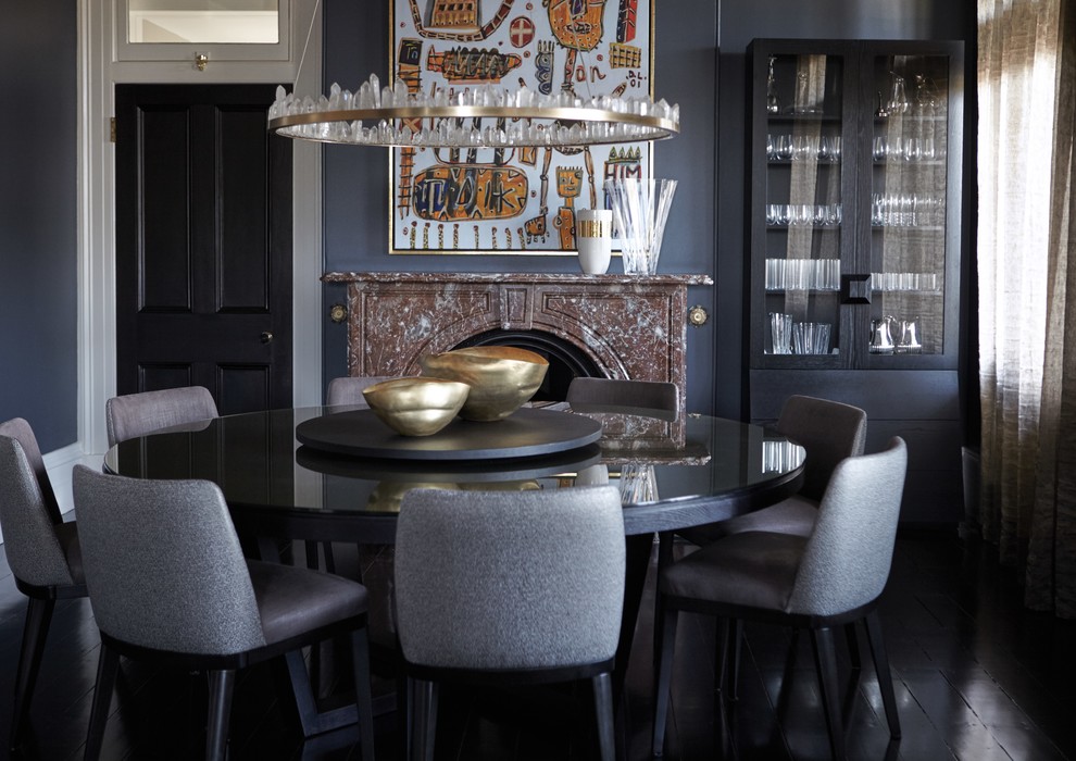 Cette photo montre une salle à manger éclectique fermée avec un mur gris, parquet peint, une cheminée standard, un manteau de cheminée en pierre et un sol noir.