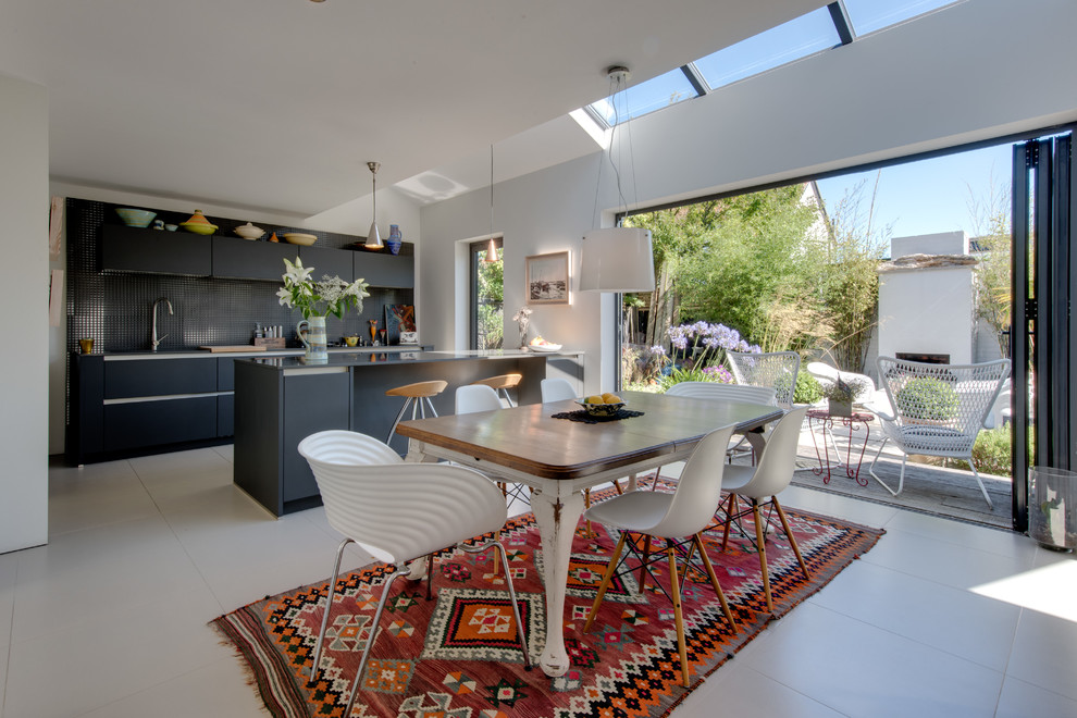 Cette image montre une salle à manger ouverte sur la cuisine bohème avec un mur blanc, un sol blanc et éclairage.