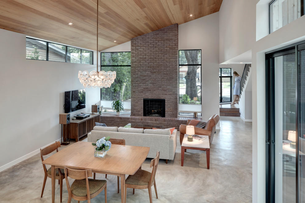 Medium sized modern kitchen/dining room in Austin with white walls, concrete flooring, a standard fireplace, a brick fireplace surround and grey floors.