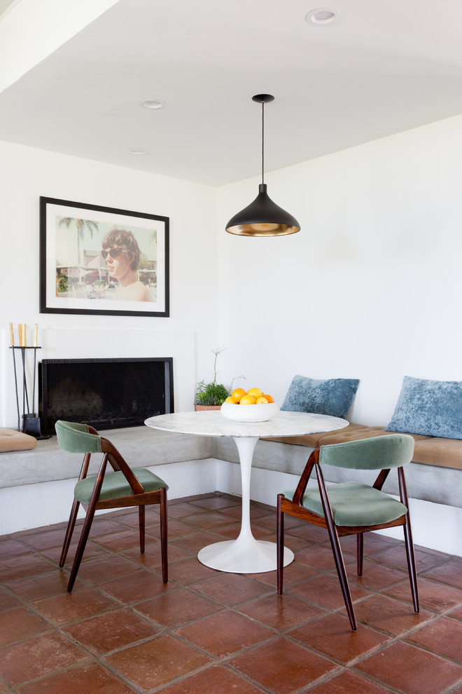 Ispirazione per una sala da pranzo aperta verso la cucina minimalista con pareti bianche, pavimento in terracotta, camino classico e pavimento marrone
