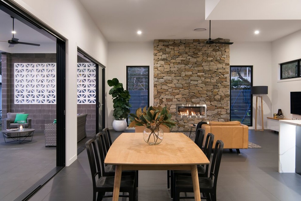 Идея дизайна: гостиная-столовая в современном стиле с белыми стенами, горизонтальным камином, фасадом камина из камня и серым полом