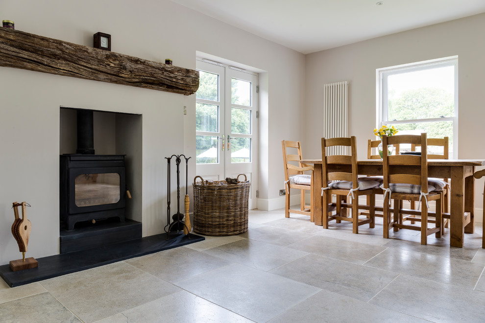 Exemple d'une grande salle à manger ouverte sur le salon chic avec un mur blanc, un sol en carrelage de céramique, un poêle à bois, un manteau de cheminée en pierre et un sol gris.