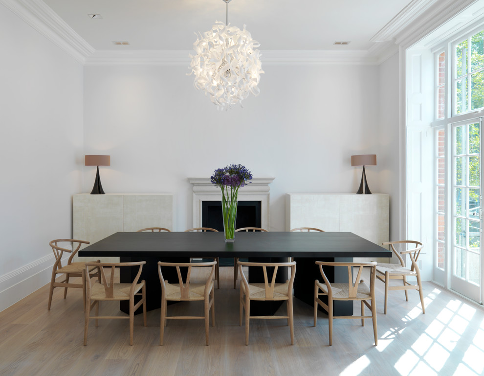 Inspiration pour une salle à manger design avec un mur blanc, parquet clair, une cheminée standard et éclairage.