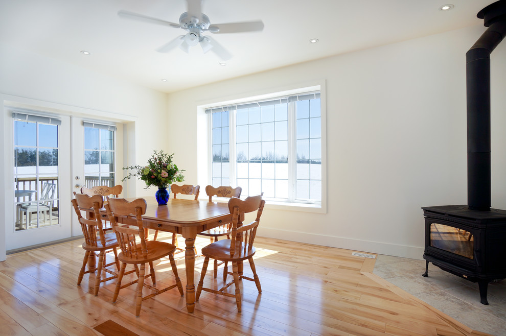 Cette photo montre une salle à manger ouverte sur la cuisine nature de taille moyenne avec un mur blanc, parquet clair et un poêle à bois.